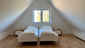 Een slaapkamer met een schuine kap, een raam met uitzicht op bomen, twee bedden, nachtkastjes en een radiator.
