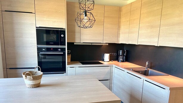 Een moderne keuken met houten kastjes, een inbouwoven, een koffiezetapparaat en een hanglamp.