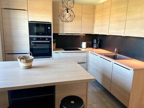 Eine moderne Küche mit Holzausstattung, einem Einbauofen, einer Kaffeemaschine und einer Pendelleuchte.