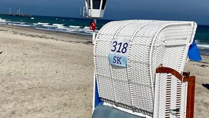 Une chaise de plage avec une pancarte indiquant « 318 SK », sur une plage de sable, avec une tour de surveillance en arrière-plan.