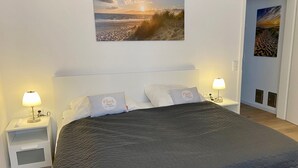 Une chambre à coucher comprenant un lit, deux lampes de chevet, une table de chevet et un tableau représentant une scène de plage, accroché au mur.