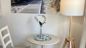 Une pièce avec une chaise blanche, une petite table ronde sur laquelle est posé un vase de fleurs et une lampe.