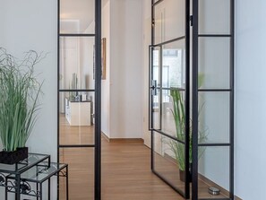 Un couloir avec des cloisons en verre, un plancher en bois et des plantes en pot.