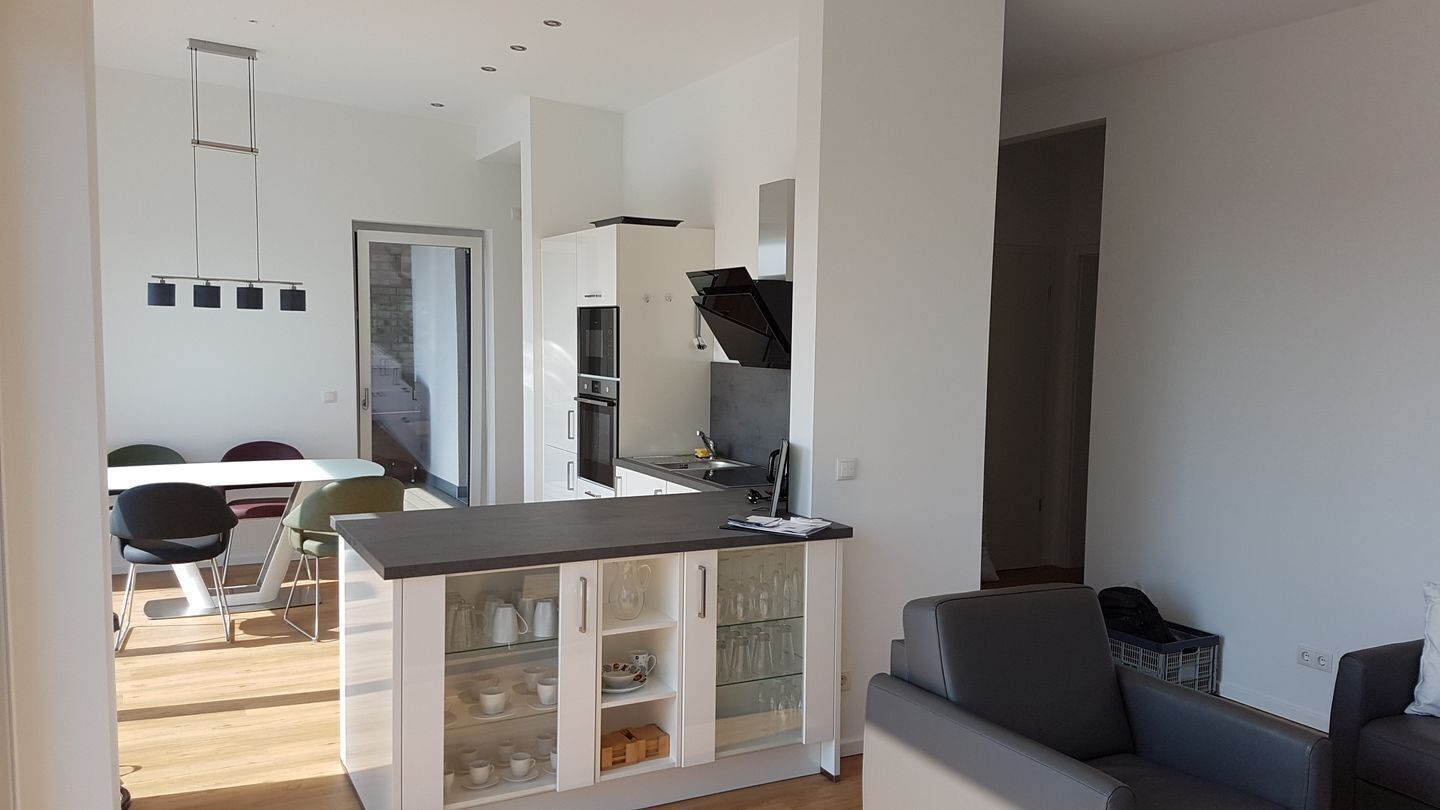 Eine moderne Küche mit weißen Schränken, einer dunklen Arbeitsplatte und einem Essbereich mit Tisch und Stühlen.