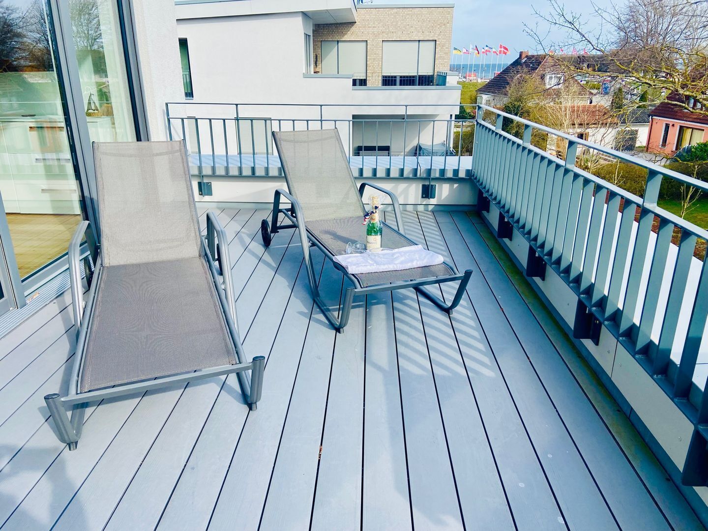 Un balcón moderno con una mesa de metal y dos sillones, con vistas a una zona residencial.