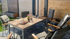 An outdoor patio with a wooden table, chairs, and a small garden area with planters.