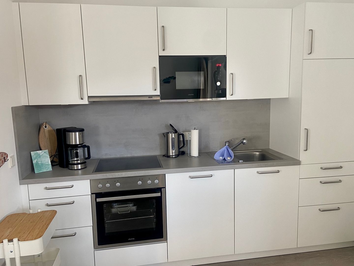 Una cocina moderna con armarios blancos, horno empotrado, cafetera y microondas.