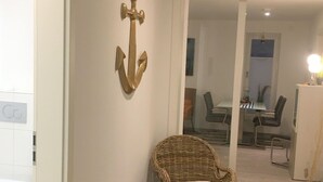 A wicker chair with a cushion in a hallway with a wall-mounted anchor decoration.