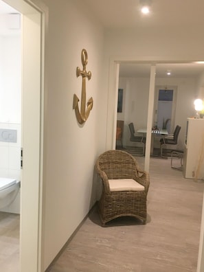 A wicker chair with a cushion in a hallway with a wall-mounted anchor decoration.