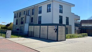 A modern multi-story building with a flat roof, large windows, and a gated entrance.