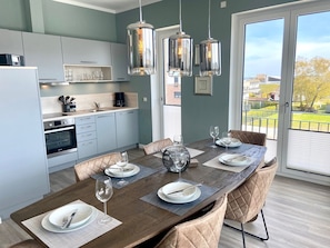 Una cocina moderna con zona de comedor, que incluye una mesa grande dispuesta para cuatro personas, una cafetera y vistas al exterior.