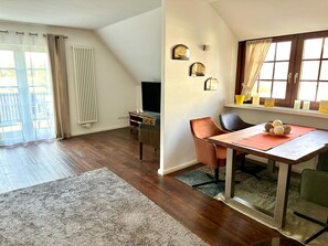 Una sala de estar acogedora con suelo de madera, una mesa de comedor con sillas, un televisor y una ventana con cortinas.