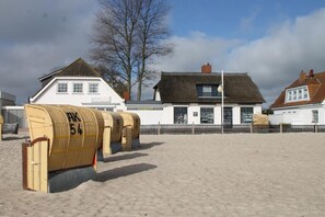 Un edificio frente a la playa con fachada blanca y techo de paja.