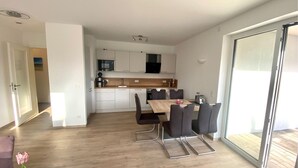 A modern kitchen with white cabinets, a wooden countertop, and a dining area with a table and chairs. - 2803 - Strandliebe - Apartment Strandliebe (Dahme)