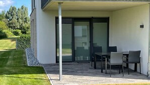 A modern patio with a table and chairs, a glass door leading to a covered area, and a well-maintained lawn. - 2803 - Strandliebe - Apartment Strandliebe (Dahme)