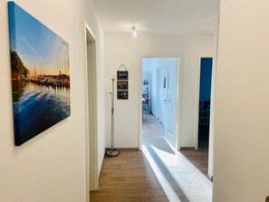 A hallway with a wooden floor, a painting of a waterfront scene, and a floor lamp. - 2803 - Love of the Beach - "Love of the Beach" Apartment (Dahme)