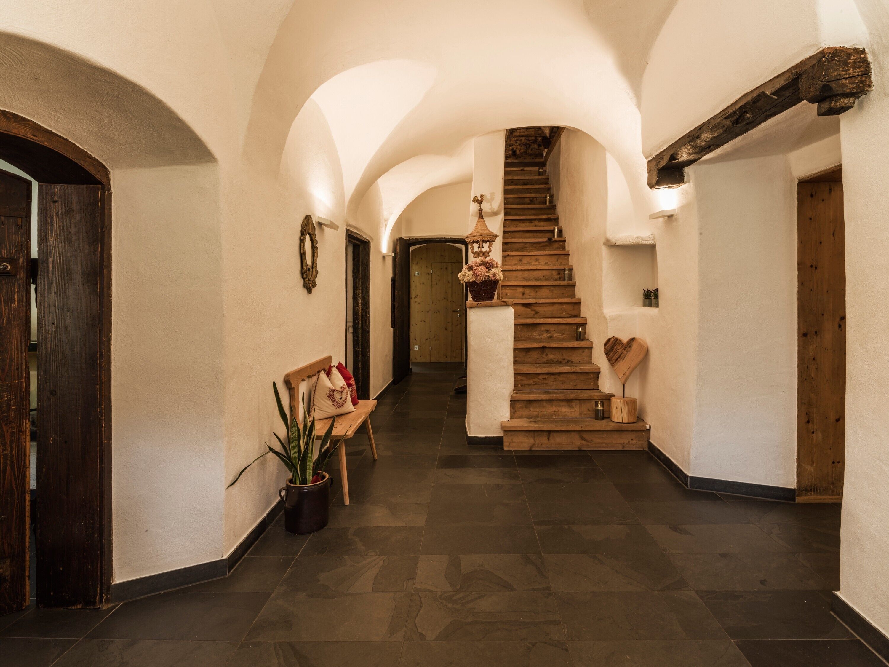 A hallway with a wooden staircase, a bench with cushions, a potted plant, and a wall-mounted decorative item.