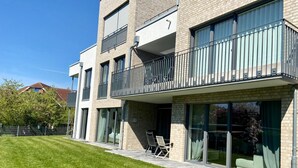 Een modern meerlaags woongebouw met balkons, grote schuifdeuren en een verzorgd gazon.