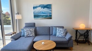 Een moderne woonkamer met een grijze modulaire bank, een ronde houten salontafel en een schilderij van een zeilboot op zee.