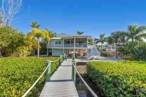 A coastal house with a covered porch, a staircase leading to a balcony, and a wooden walkway surrounded by greenery. - Pool home on Bocilla Lagoon (Placida)