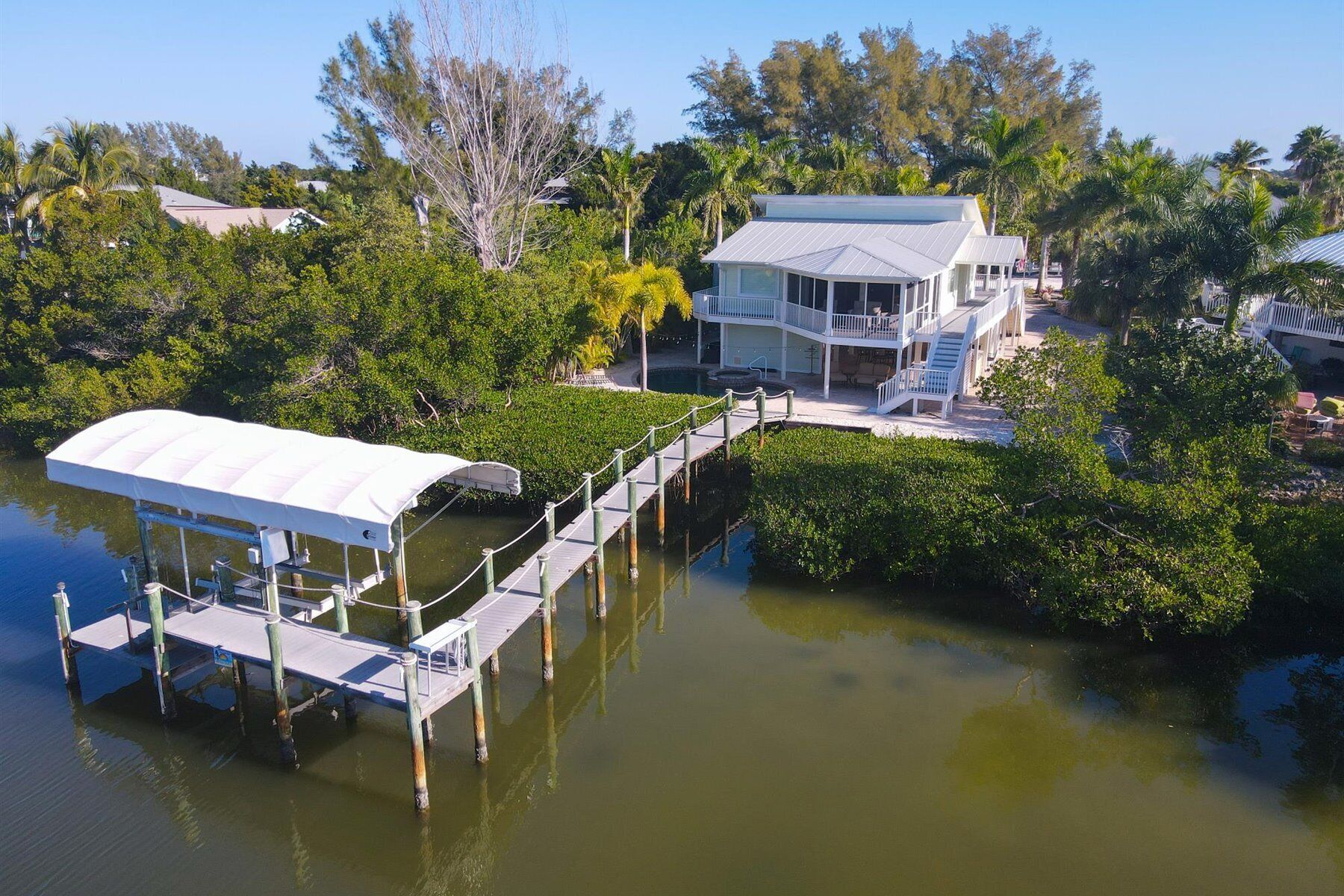 A waterfront property with a covered dock, a house with a balcony, and lush greenery.