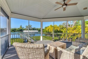 A covered outdoor area with a wooden deck, wicker furniture, and a view of a lake and trees. - Pool home on Bocilla Lagoon (Placida)