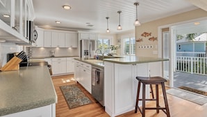 A modern kitchen with white cabinets, a large island, stainless steel appliances, pendant lighting, and a view of the outdoors. - Pool home on Bocilla Lagoon (Placida)