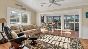 A spacious living room with a ceiling fan, a leather chair, a sofa, and a dining table with chairs. There are large windows and a sliding glass door leading to an outdoor area. - Pool home on Bocilla Lagoon (Placida)