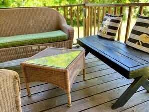 Una silla de mimbre con cojín verde y una mesa con cubierta de vidrio sobre una terraza de madera.
