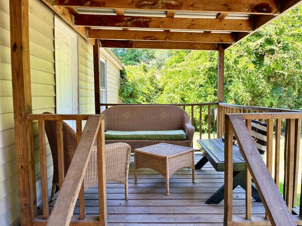 Relax on the deck with a wicker sofa and table under a pergola, surrounded by a lush garden.