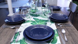 Une table à manger dressée avec de l’argenterie, des verres à vin et des assiettes bleues, le tout recouvert d’une nappe ornée d’un motif de feuilles vertes.