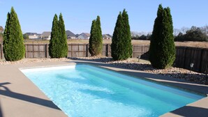 Une piscine rectangulaire à l’eau d’un bleu limpide, entourée d’une terrasse en béton et d’une clôture en bois.