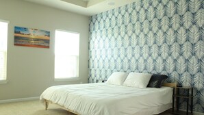 Une chambre à coucher avec un lit, une table de chevet, un mur orné d’un motif de feuilles et une fenêtre.