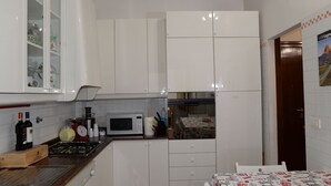 A compact kitchen with white cabinets, a microwave, a stove, and a dining area with a table and chairs. - Emilio's Home Entire Apartament up to 7 people (Roma)