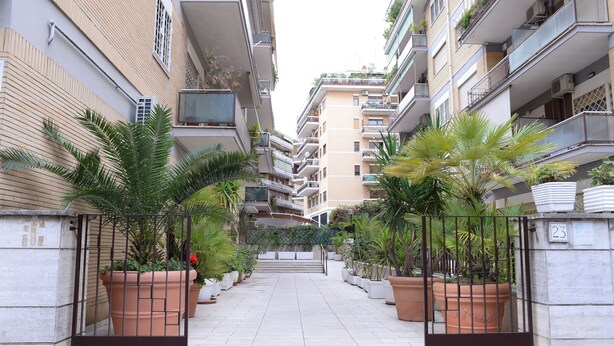 A residential building with multiple balconies, a gated entrance, and potted plants along the pathway. - Emilio's Home Entire Apartament up to 7 people (Roma)