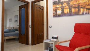 A room with a bed, a red chair, a small table with a magazine, and a painting of a bridge. - Emilio's Home Entire Apartament up to 7 people (Roma)