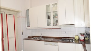 A kitchen with white cabinets, a double sink, a stove, and a small refrigerator. - Emilio's Home Entire Apartament up to 7 people (Roma)