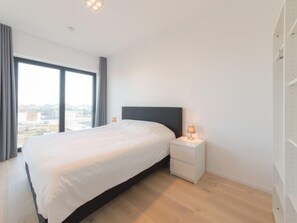 A modern bedroom with a large bed, a nightstand, and a window offering a city view.