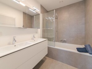 A modern bathroom with a large white sink, a glass-enclosed shower, and a bathtub.