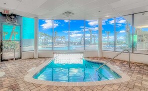 An indoor swimming pool with clear views of palm trees and a blue sky through large windows.