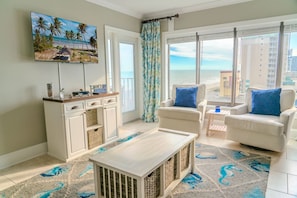 A living room with a TV, a sofa, a coffee table, and a view of the beach.