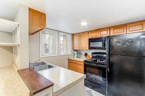 Modern kitchen with a stainless steel sink, black appliances, and wooden cabinets.