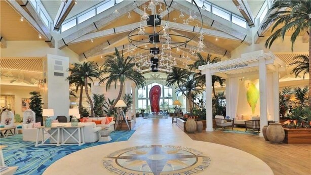 Een ruime lobby met een hoge plafond, palmbomen en een kroonluchter in het midden.