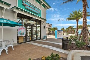 Une boutique de la chaîne Bahama's Original Shaved Ice, avec une devanture en verre transparent, des places assises à l'extérieur et un panneau indicateur.