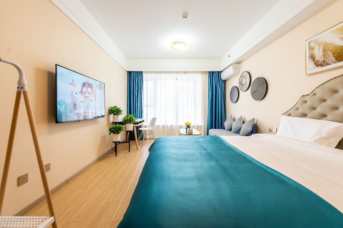 A hotel room with a bed, a desk, a chair, a TV, and a window with curtains.