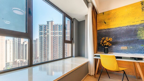 Een moderne kamer met een groot raam, een gele stoel en een schilderij aan de muur.