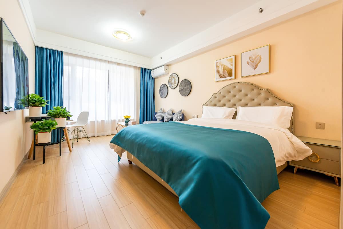 A modern bedroom with a large bed, a desk with a chair, and a window with curtains.