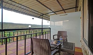 A balcony with wicker chairs, a table, and a bottle of water. - Treebo Berry Hill Venna Lake, 3 Km From City Center (Mahabaleshwar)