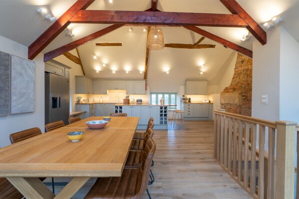 Enjoy meals in this inviting dining area with a long table and staircase leading to an upper level.