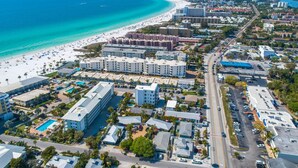 An aerial view of a coastal city with a beach, hotels, and roads.